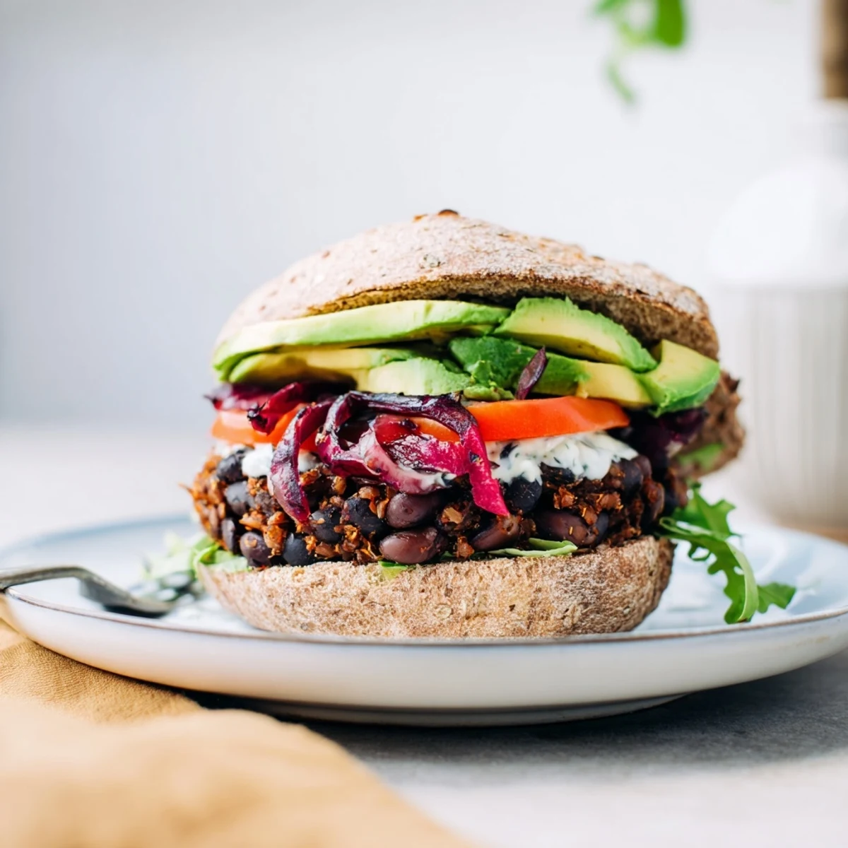 A close-up of a flavorful zesty black bean burger, stacked high with avocado and fresh vegetables.