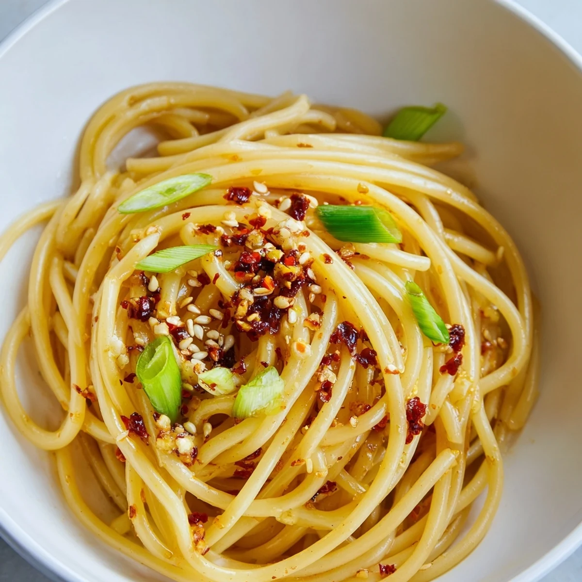 Steaming bowl of Garlic Chili Oil Noodles with bright green scallions and sesame seeds.