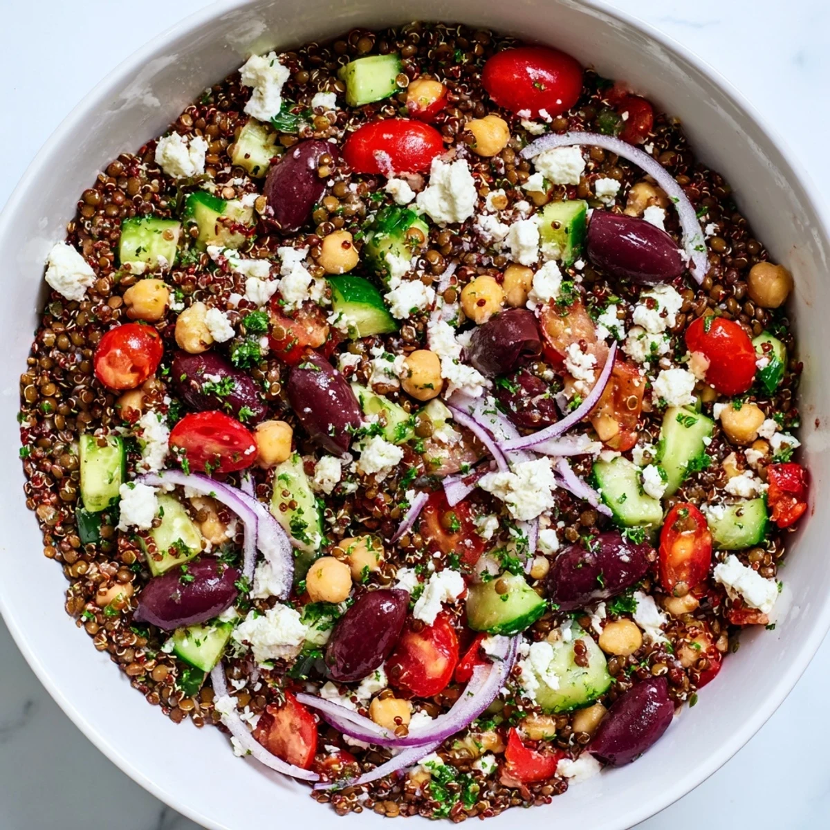 Fork-tender lentils, quinoa, and chickpeas are tossed with crisp veggies in a Greek Power Salad, ready to serve.