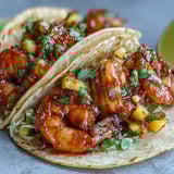 Spicy Sriracha Shrimp Tacos with Mango Salsa are topped with crunchy cabbage and fresh lime wedges on a platter.
