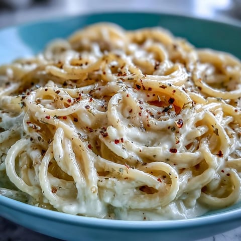 Golden strands of Cacio e Pepe pasta twirled on a fork, coated in a creamy Pecorino Romano sauce with visible freshly cracked black pepper.
