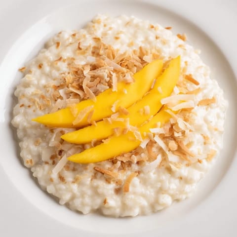 Creamy Toasted Coconut Rice Pudding, garnished with golden coconut flakes and ripe mango slices, a dessert.