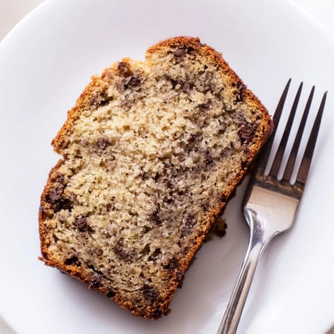 Golden-brown banana bread cooling on a wire rack, with sliced pieces showcasing chopped walnuts and a soft, fluffy texture for a perfect breakfast snack.
