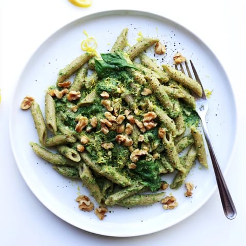 A close-up shot of Creamy Spinach Walnut Pasta twirled on a fork, showing the velvety, plant-based sauce clinging to each noodle.