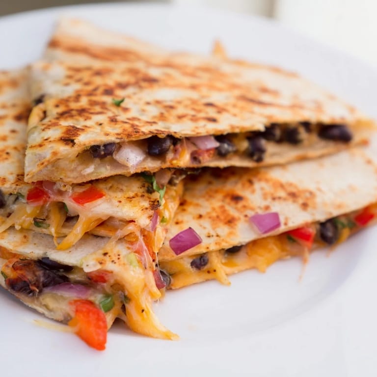 A close-up shot of a Black Bean Quesadilla, showing the cheesy, veggie-packed filling inside.