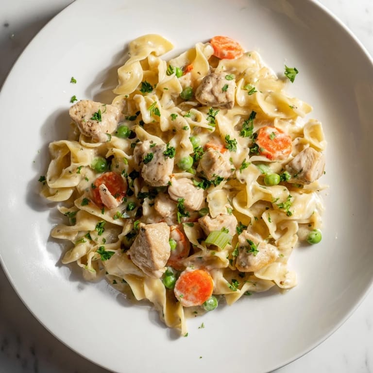 Close-up photo of creamy chicken and egg noodles, garnished with fresh parsley, looks delicious.
