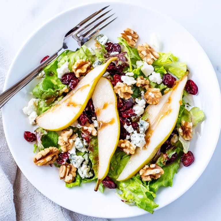 Close-up of a vibrant pear Gorgonzola salad featuring juicy fruit, creamy cheese crumbles, and toasted walnuts on a bed of fresh greens.