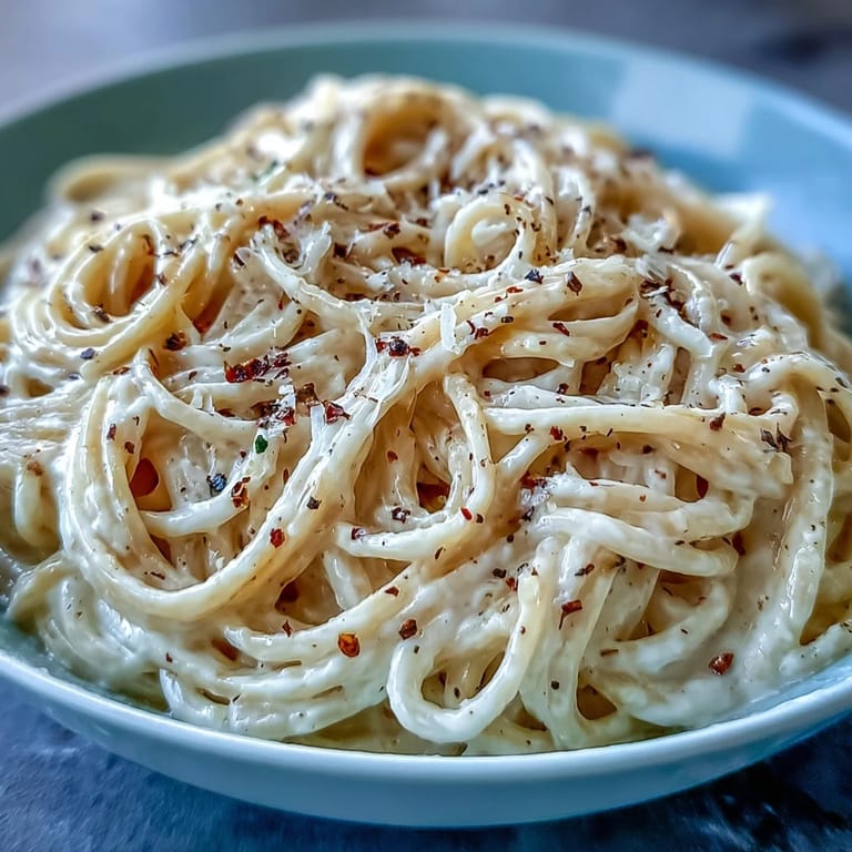 Close-up view of a serving plate showing Cacio e Pepe with extra pepper and cheese, ready to be enjoyed with a glass of white wine.