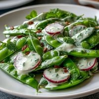 Crisp snap pea and radish salad with fresh herbs and creamy tahini dressing, ideal for a refreshing spring lunch or side dish.